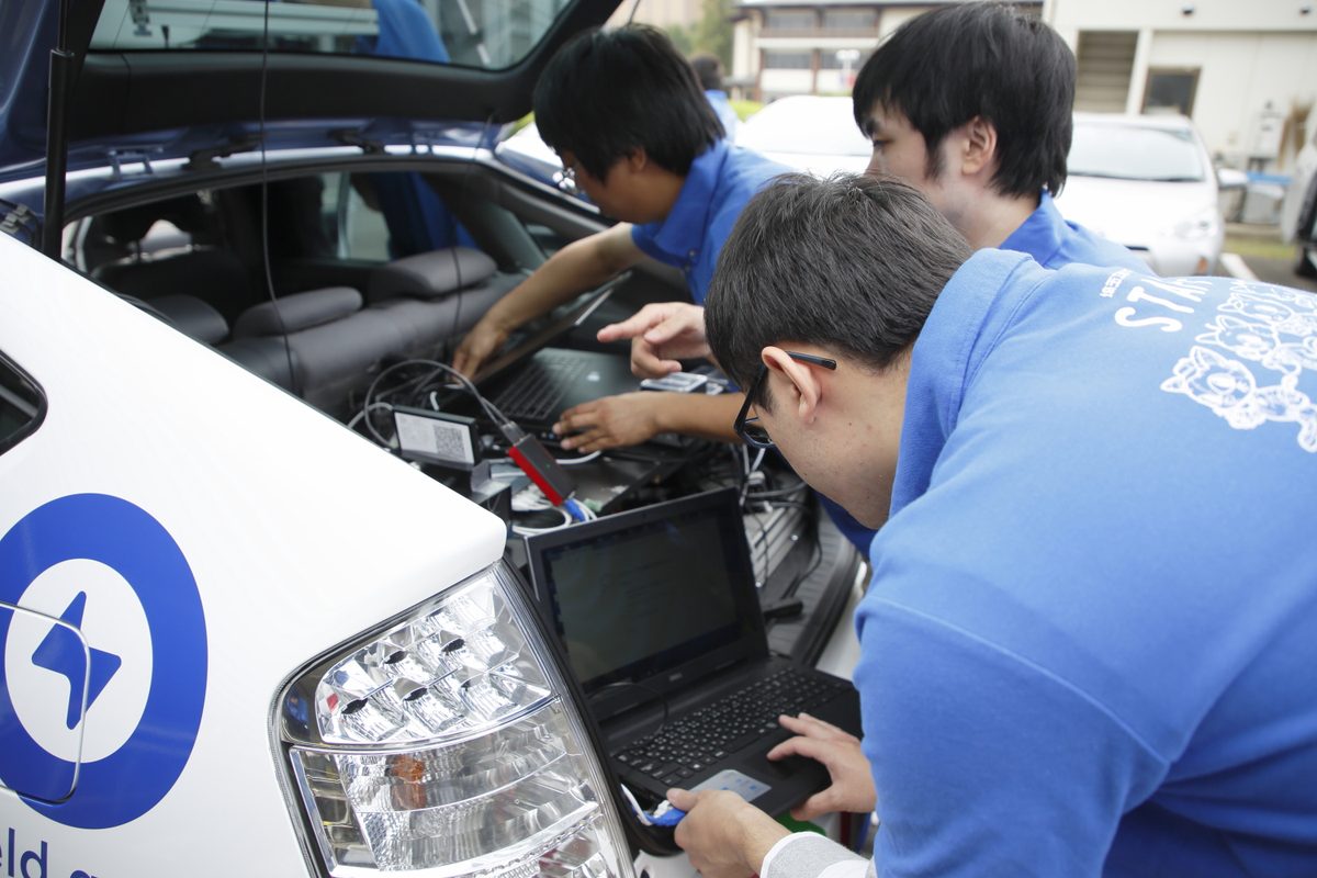 実験車のボンネットを開けてノートPCで調整する学生